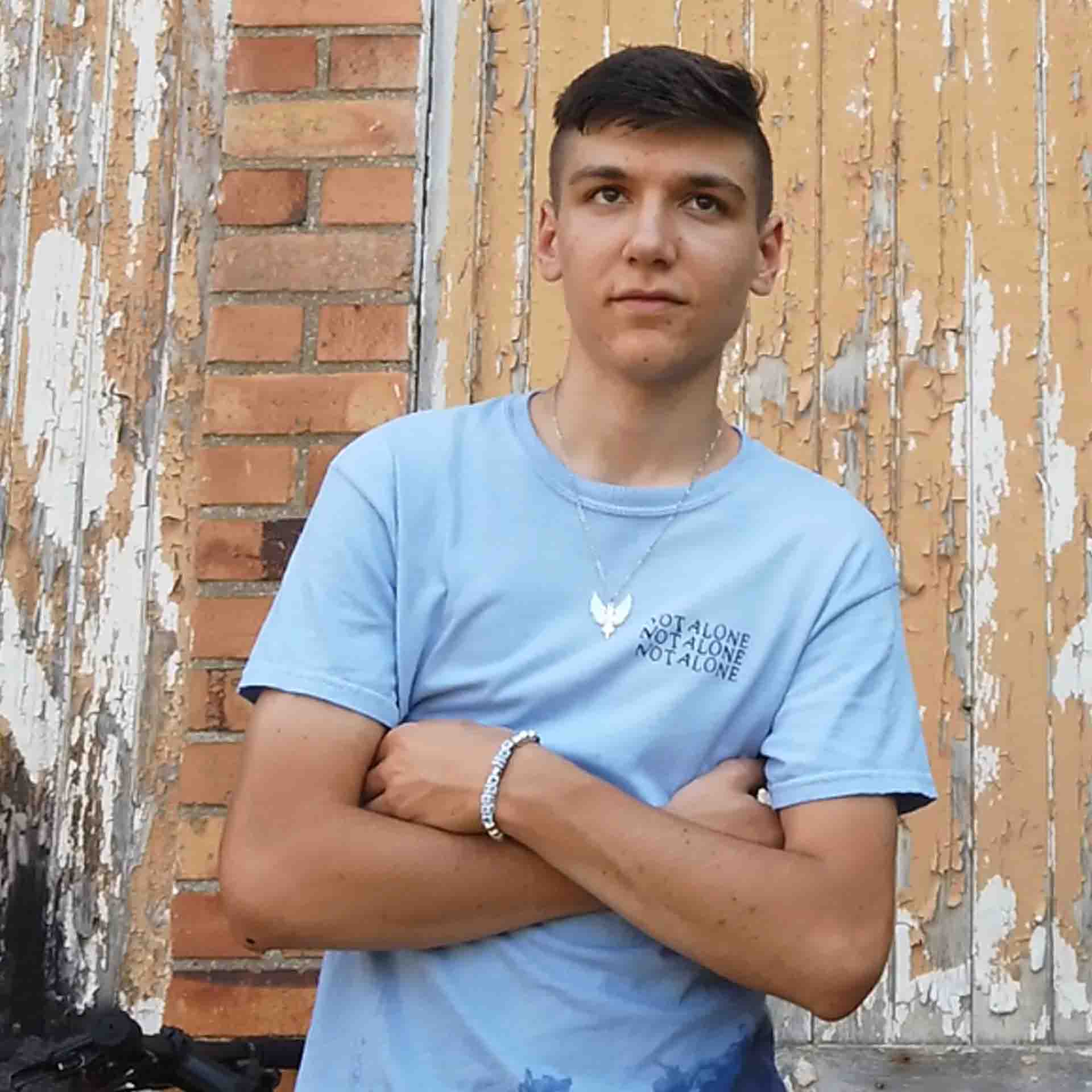NOT ALONE Shirt - handmade / Größe M / himmelblau / mit Metallpatch 2 Jugendlicher mit blauer T-Shirt vor altem, verzierten Wand mit Holz und Backstein, christliche Botschaft, Lifestyle.