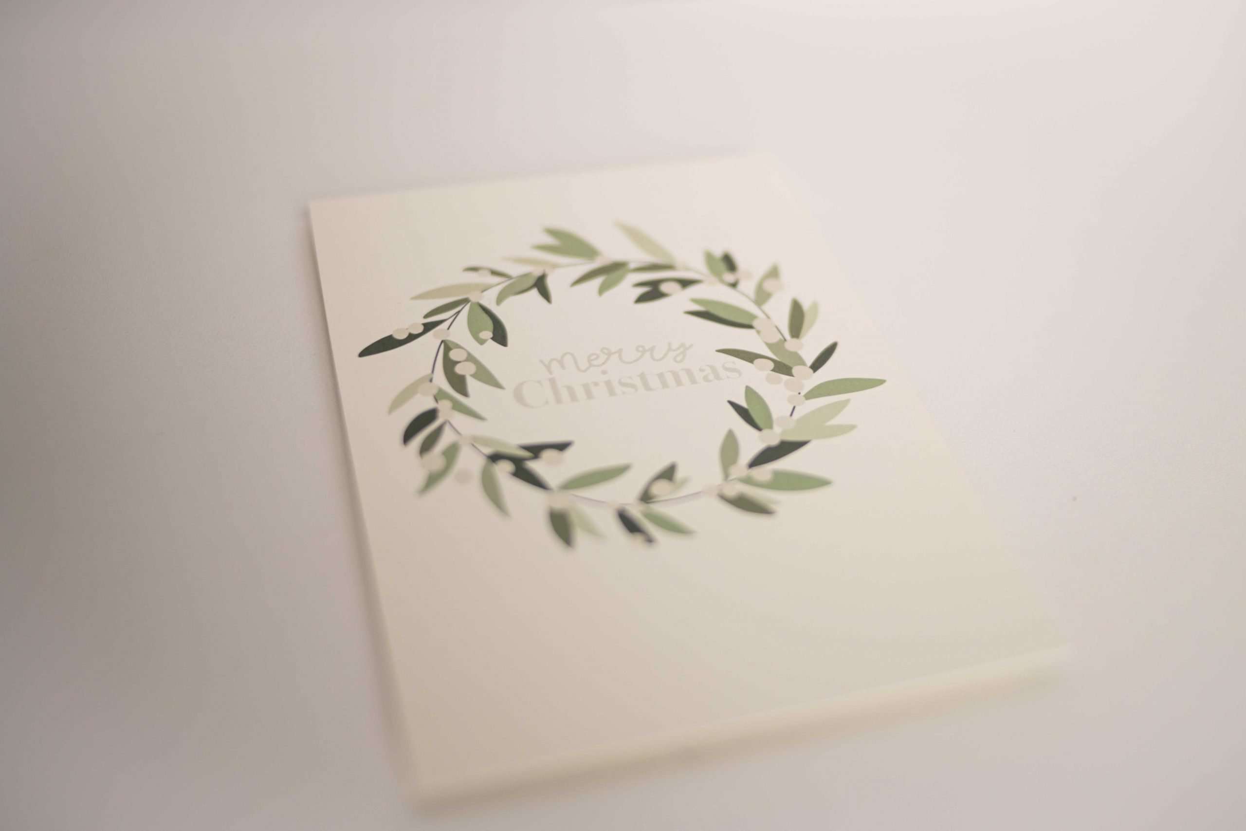 Stilvolle Weihnachtskarte mit grünem Kranz und 'Merry Christmas' Schriftzug.