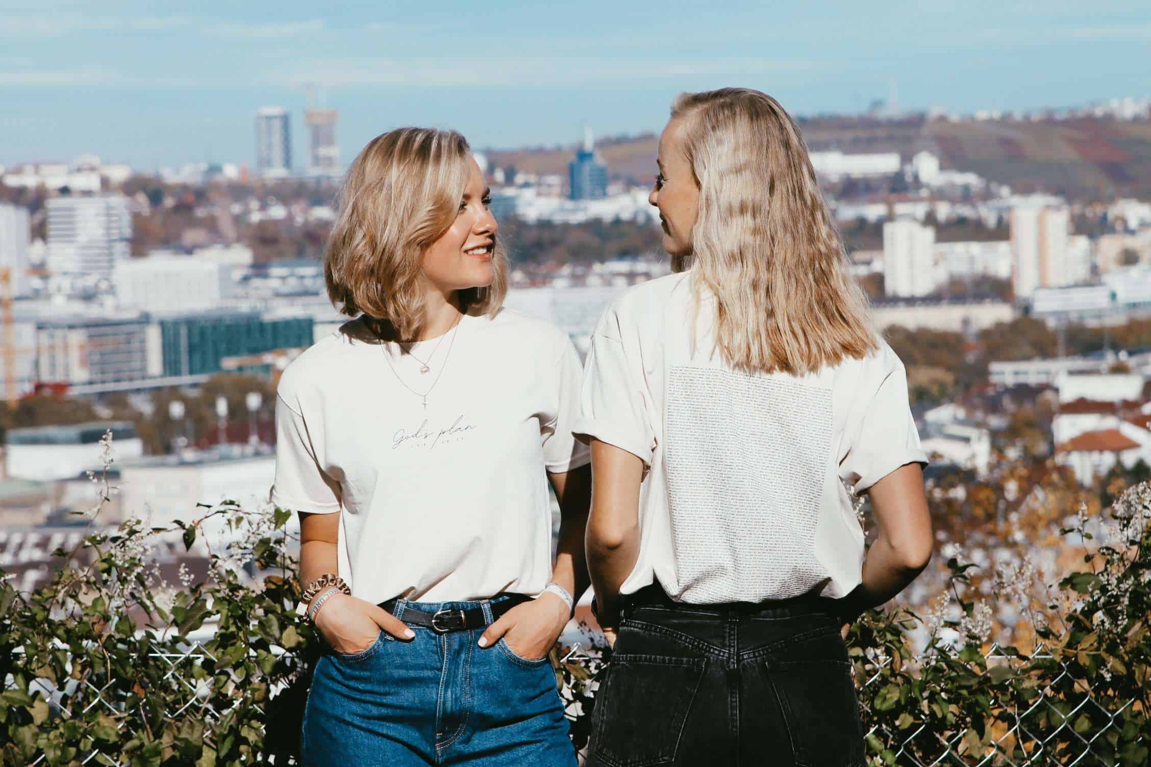 T-Shirt "God's Plan" Unisex 17 Zwei junge Frauen sprechen sich auf einer Stadtterrasse mit Blick auf die Skyline青 Lexikon erstellen, evangelische Mode, christliche Freundschaft.