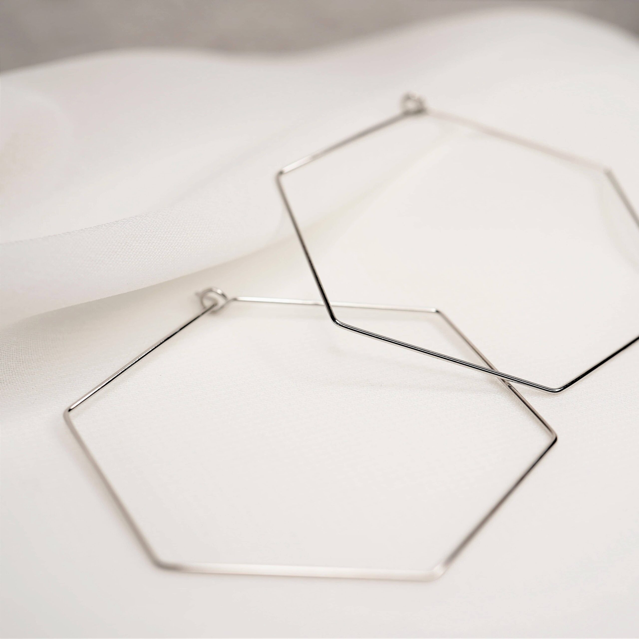 Jiska | Christliche Creole – 18k Gold beschichtet – gold/silber – nachhaltig verpackt 11 Minimalist silberne geometrische Schmuckstücke auf weißem Stoff.