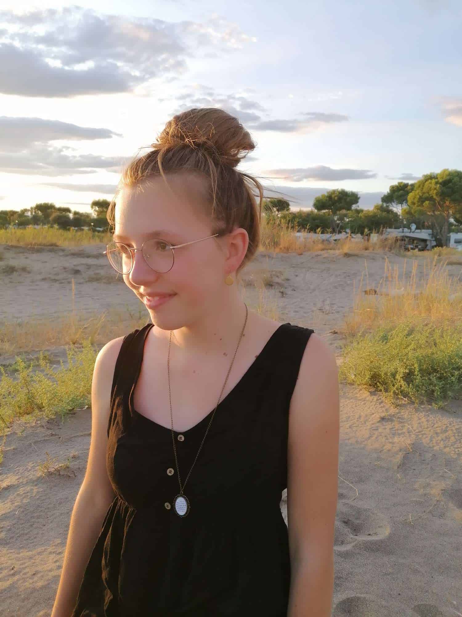 Ohrringe Goldplättchen 2 Moderne Frau mit Brille, Schmuck und schwarzen Kleid im Freien bei Sonnenuntergang.