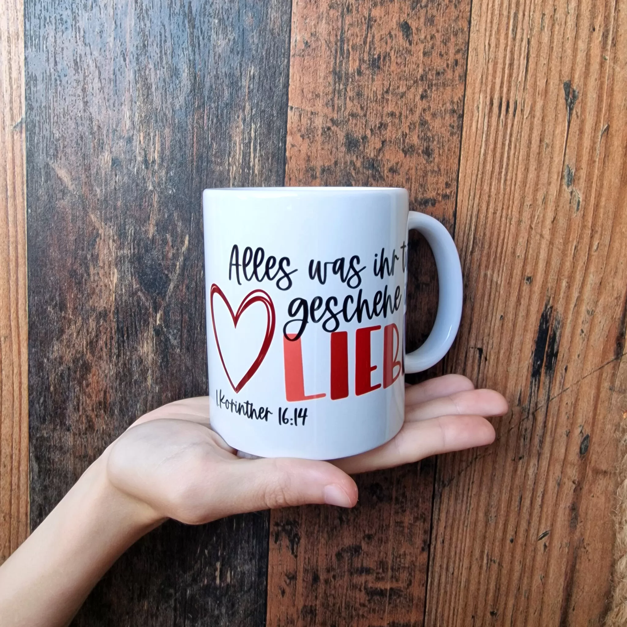 Alles, was ihr tut, geschieht in Liebe | 1. Korinther 16, 14 | Jahreslosung 2024 | Tasse 5 Weiße Tasse mit christlichem Spruch und Herz, auf Holzoberfläche.