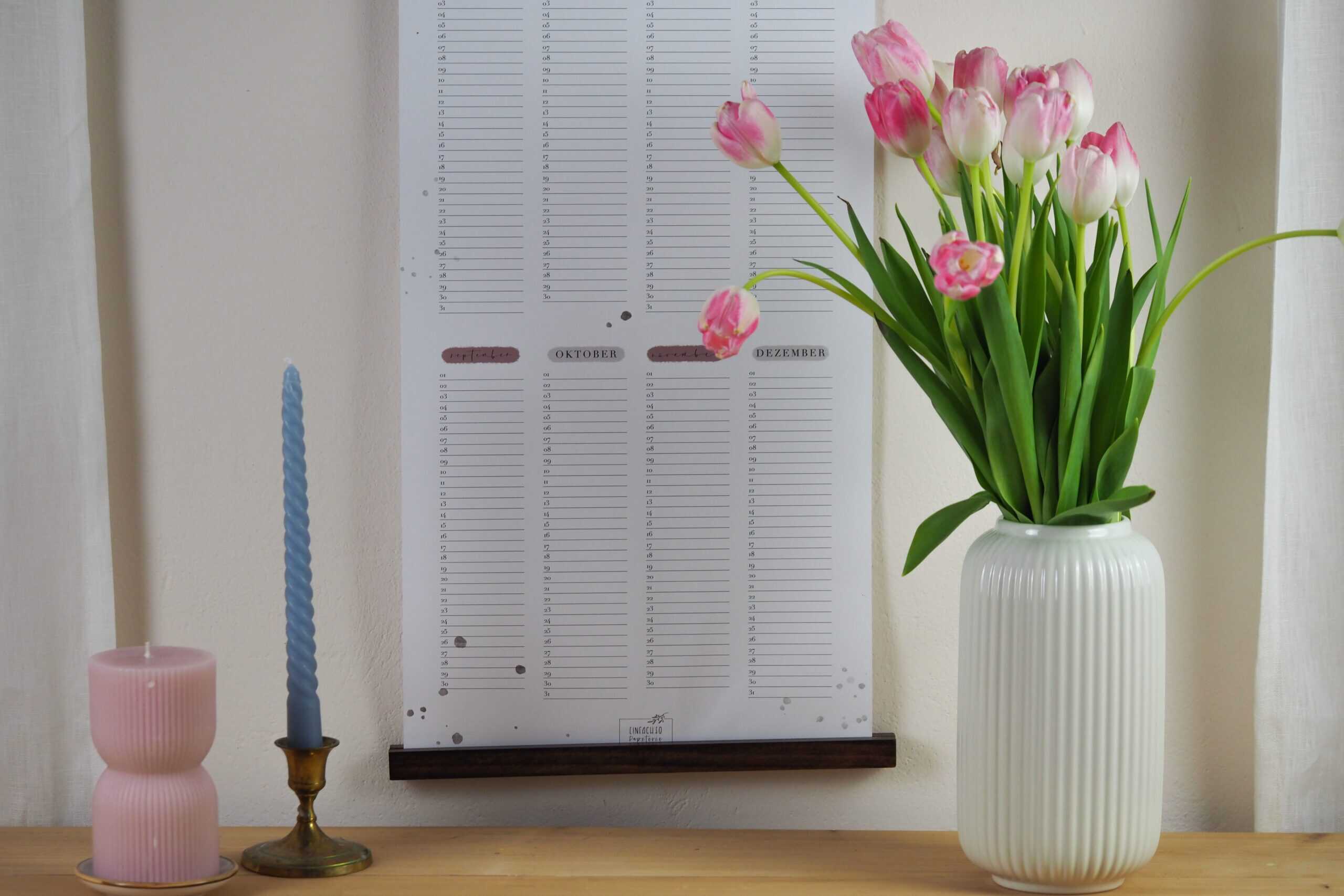 Wiederkehrender Geburtstagskalender "Viel Glück und viel Segen!" 3 Blumenstrauß mit Tulpen in weißem Vasen, Pastellkerzen und Kalender an der Wand.