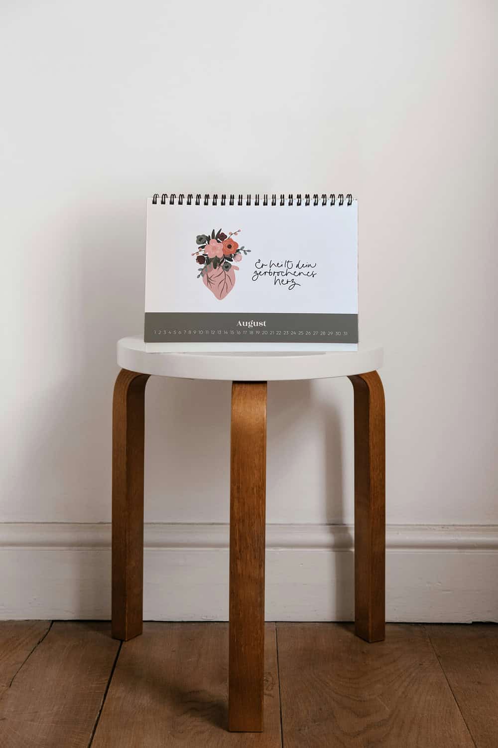 Ein christlicher Kalender "Geliebtes Kind" auf einem Holzstuhl vor weißer Wand, Gebets- und Glaubens.