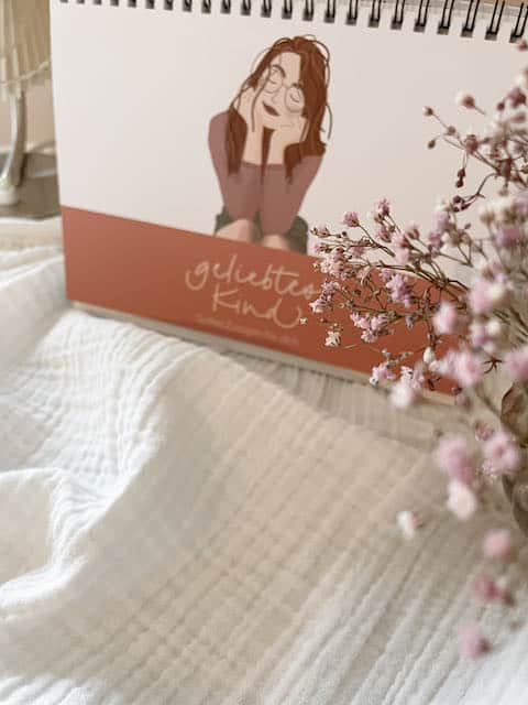 Kalender "geliebtes Kind" 3 Stoffbuch mit christlichem Motiv und Kirschblüte auf weißem Bettbezug.