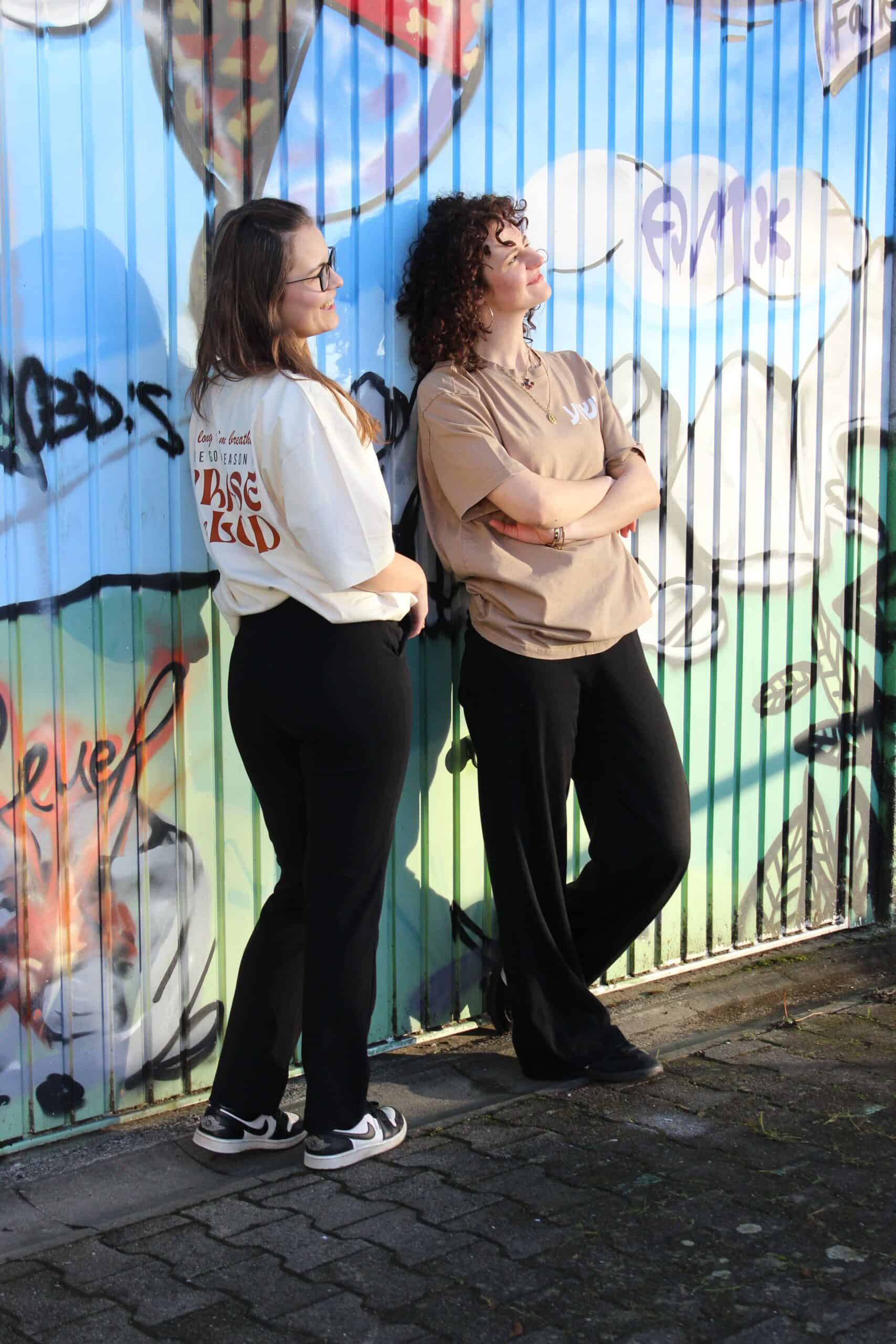 "worship" | Oversized Tshirt | Creme | Rostrot 17 Zwei Frauen mit christlichen T-Shirts vor graffiti-bemalter Wand, streetwear, christliche Mode.