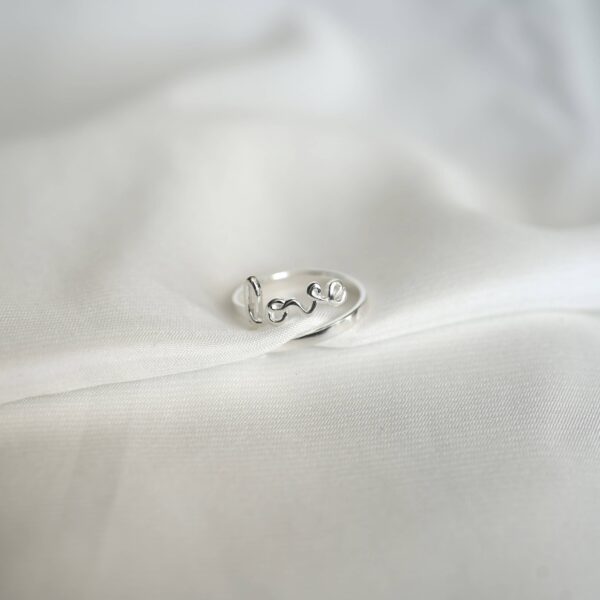 Schlichtes Love-Ring aus Silber auf weißem Stoff, christliche Schmuckmode, Geschenk für Gläubige.