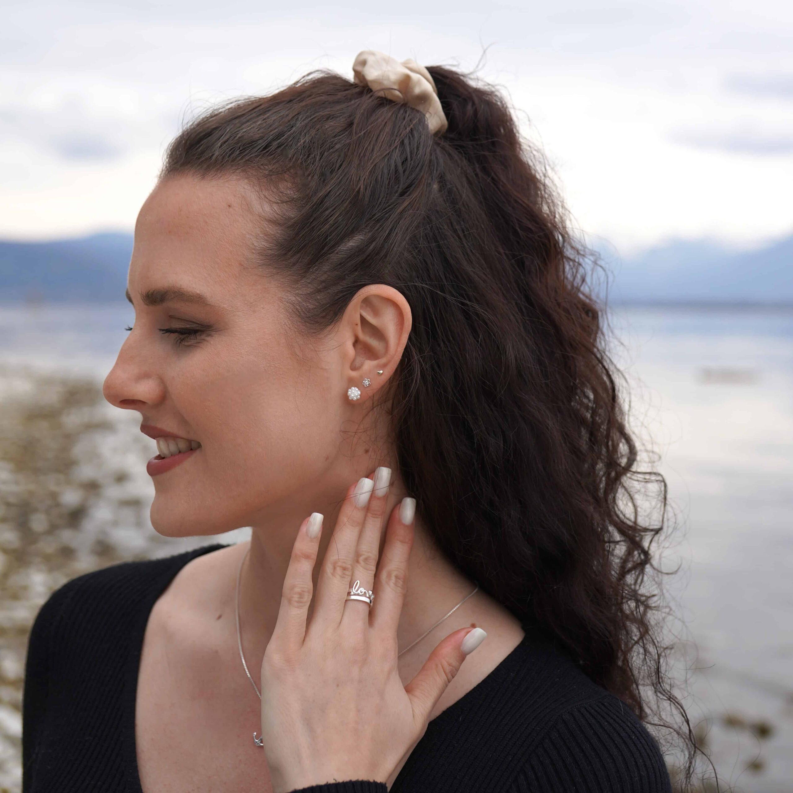 Pearl Mini | Christliche Ohrstecker – 925 Sterling Silber – 6mm Ohrstecker mit Perlen 2 Hübsche Frau mit Schmuck am See, naturverbunden, modischer Look, entspannte Stimmung.