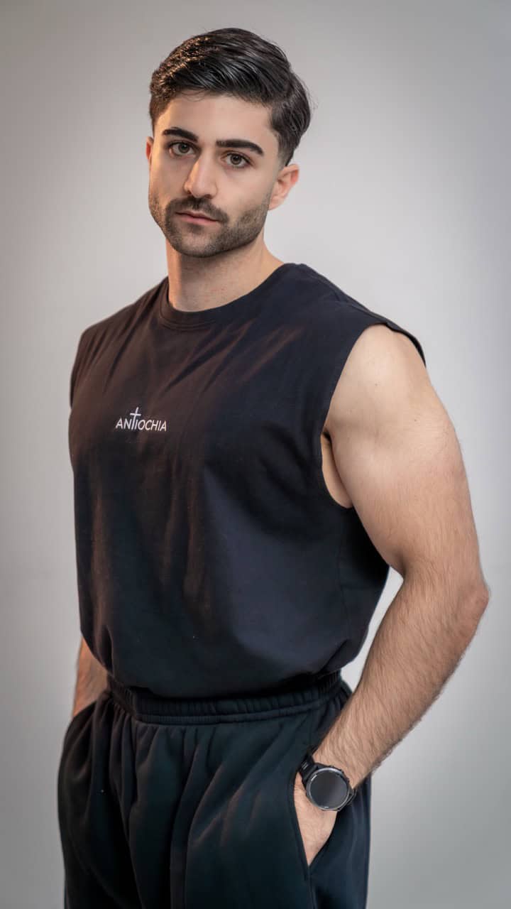 Mann in schwarzem T-Shirt mit "Antiochia" Schriftzug, christliche Mode, Glaube tragen.