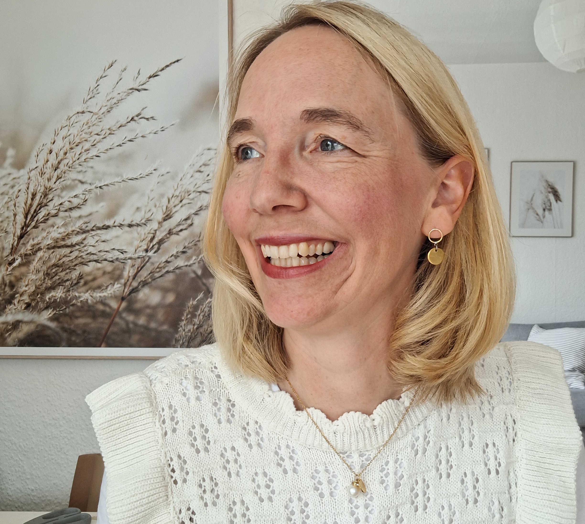Goldkette "Der dich behütet" 4 Ein lächelnde Frau mit blondem Haar, die in einem hellen Raum sitzt, christliche Marken.