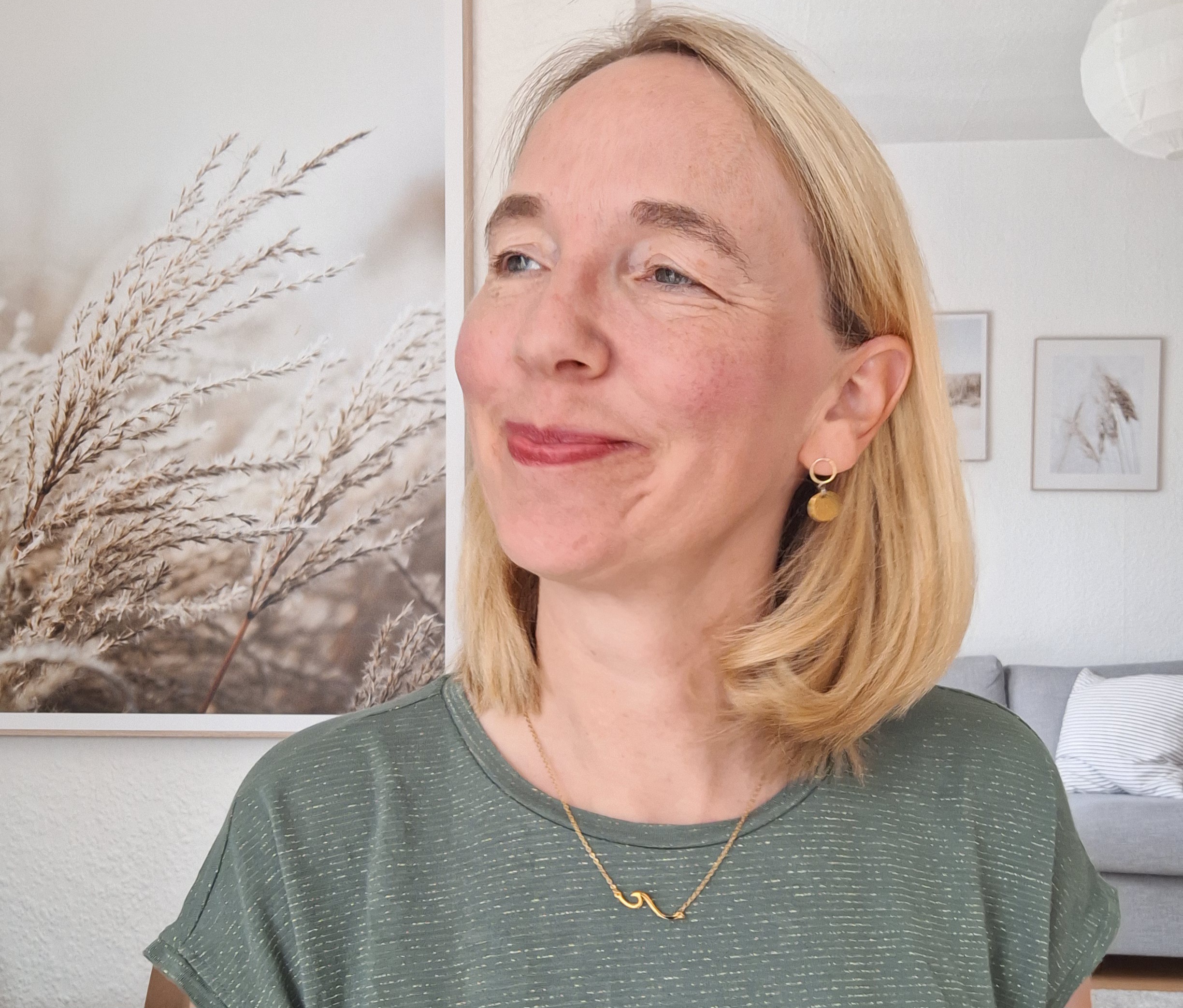 Goldkette "Welle" 3 Gebildete Frau mit blondem Haar, christliche Dekoration im Hintergrund, freundliche Atmosphäre.