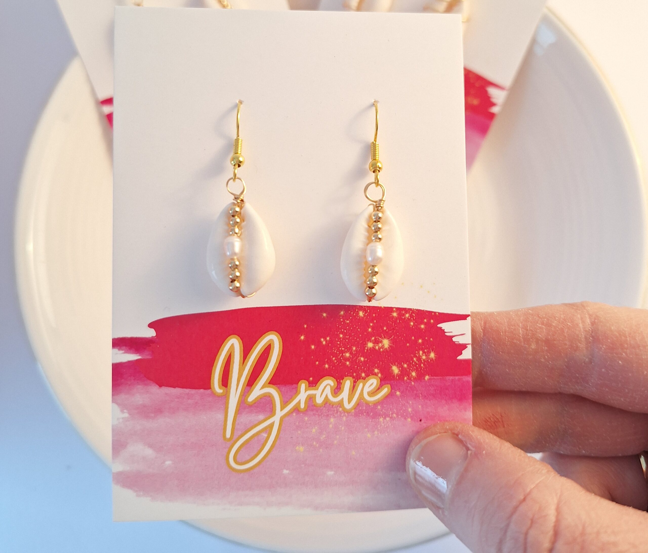 Hängende Perlenohrringe auf weißer Karte mit "Brave" Schriftzug, Schmuck, Accessoire, Geschenk.