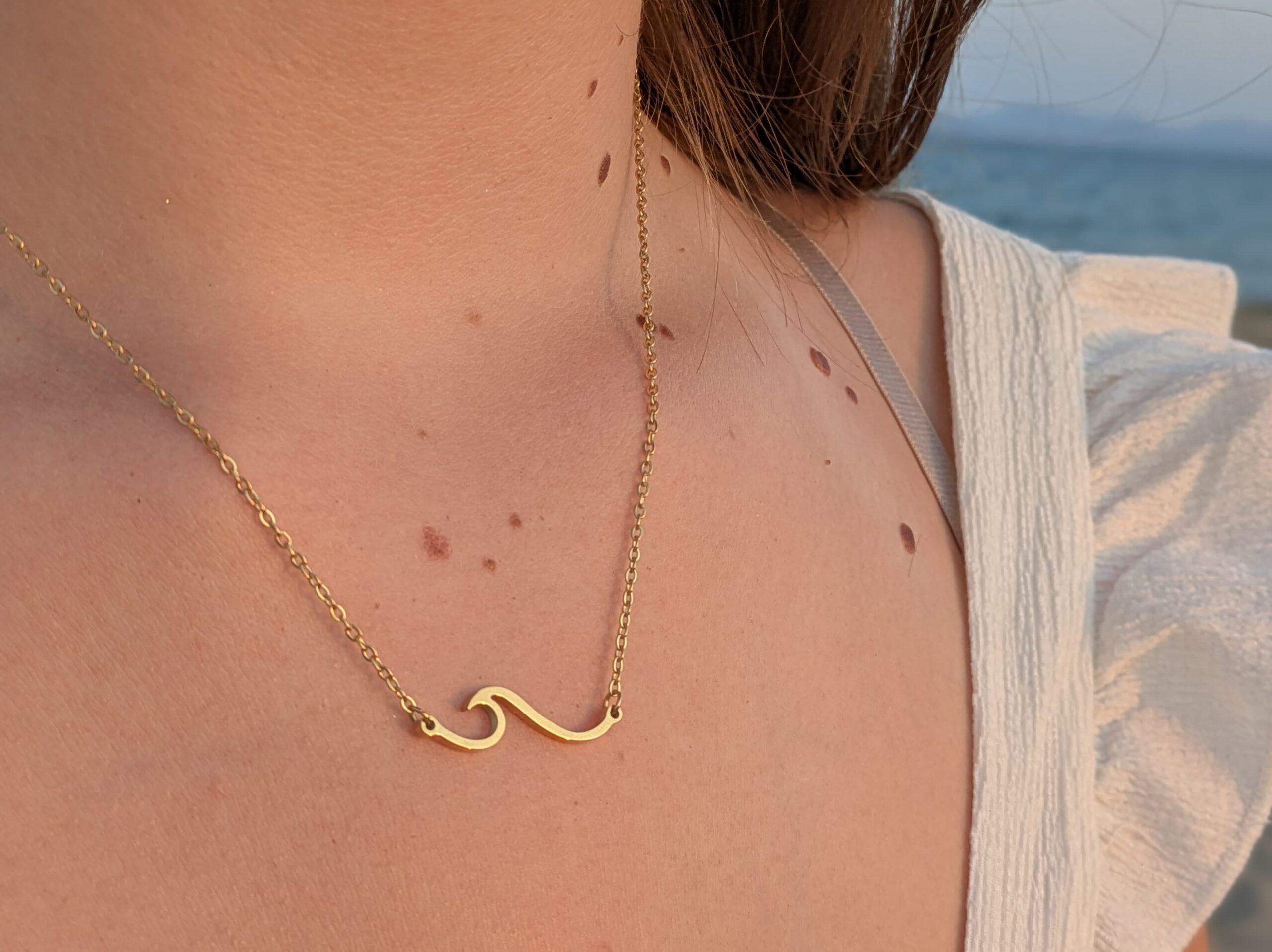 Goldkette "Welle" 4 Goldene Halskette mit Wellen-Design, Nahaufnahme, am Strand getragen.