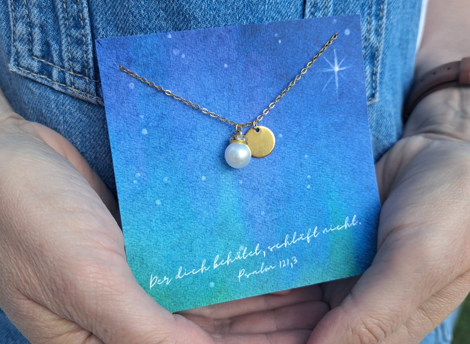 Der christliche Schmuck mit Perle und goldener Medaille auf blauer Himmelkarte.