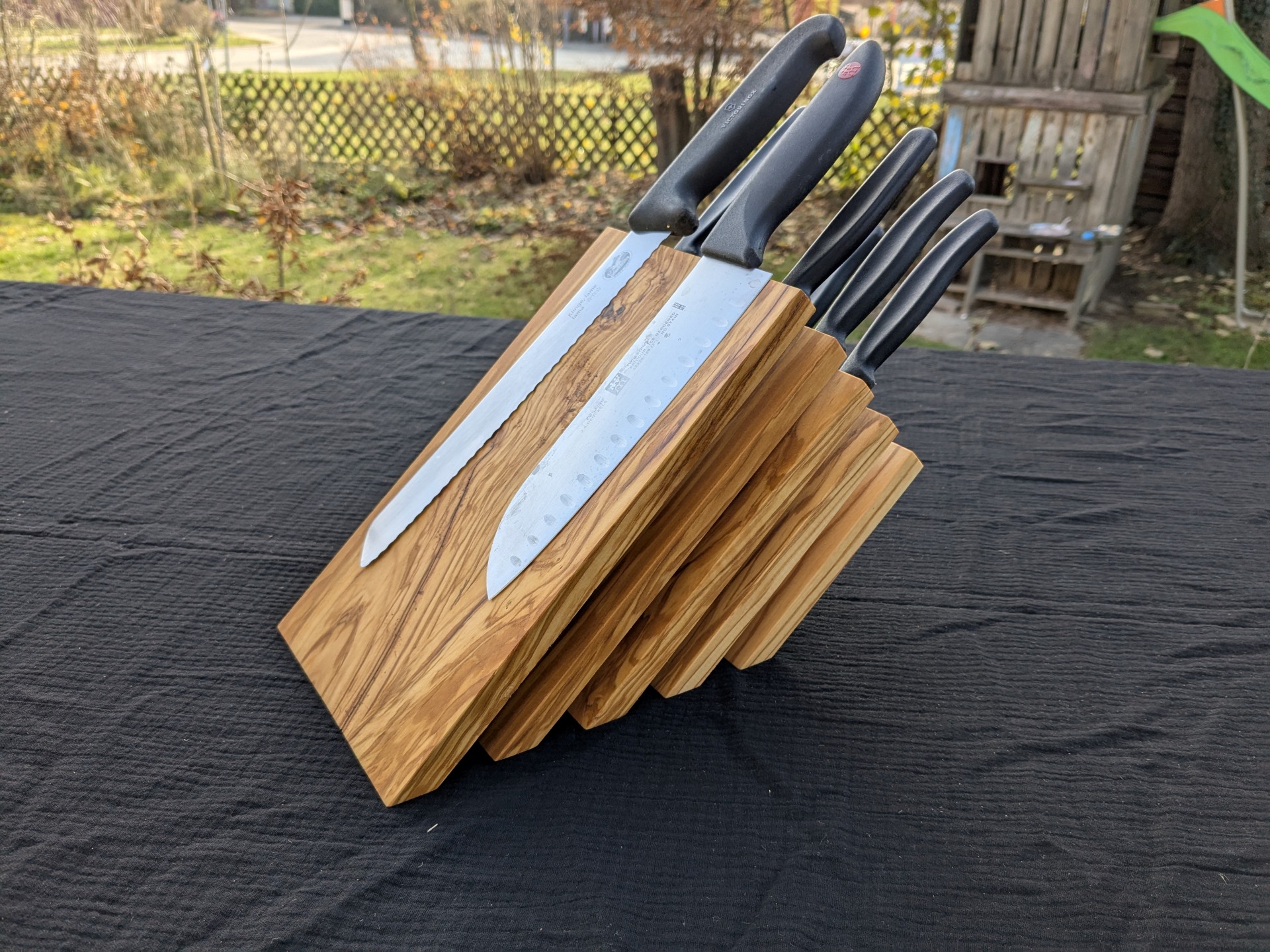 Hochwertiges Messerset aus Holz mit verschiedenen Küchenmessern auf schwarzem Tisch.