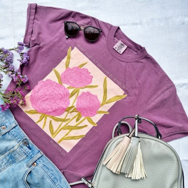 Ein stilvolles lila T-Shirt mit Blumenmuster, Sonnenbrille und Handtasche, christliche Mode.