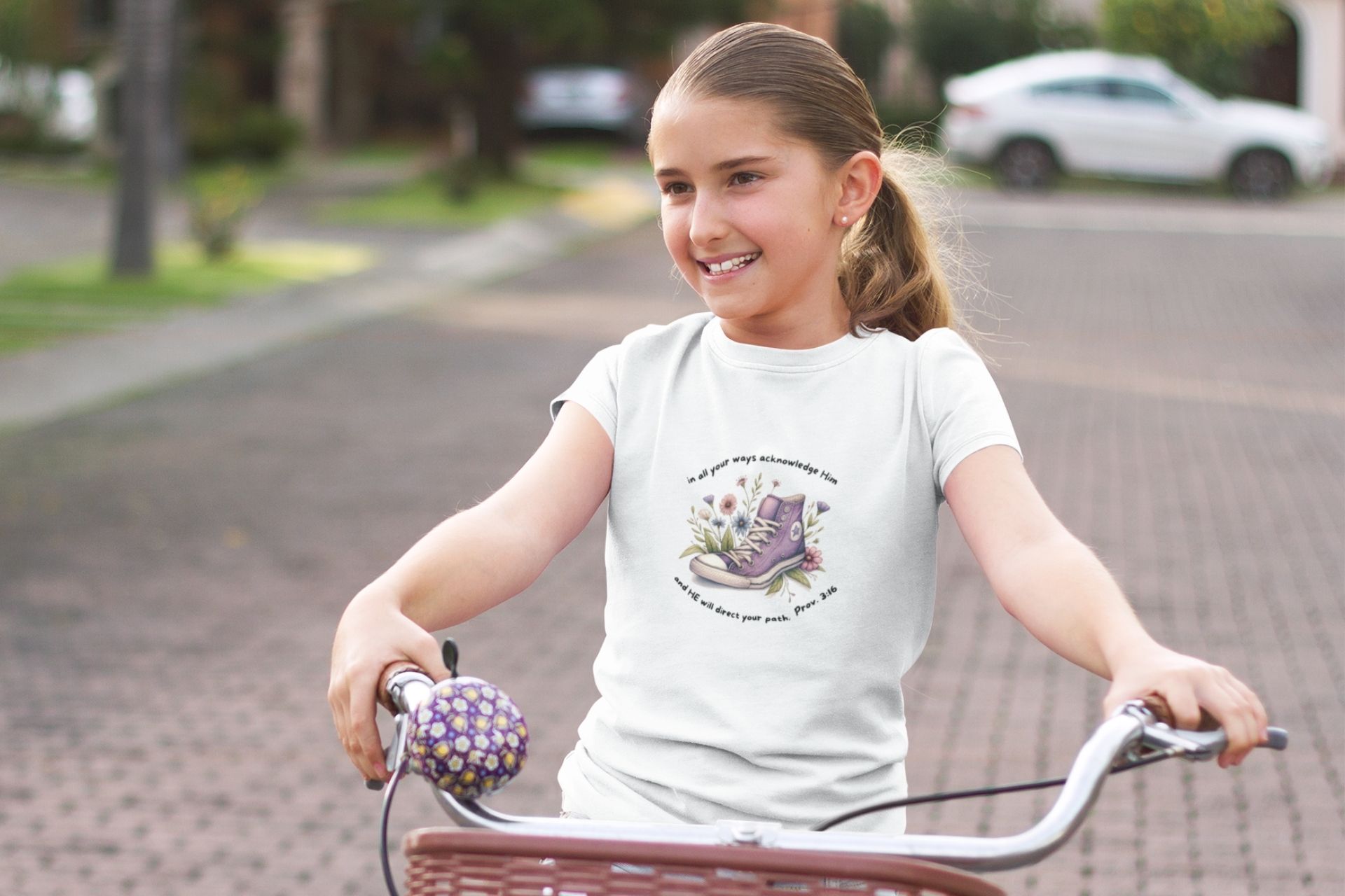 Sprüche 3,16 Sneaker süßes Girls Bio-Baumwolle T-Shirt 12 Ein Mädchen fährt Fahrrad mit einem weißen T-Shirt, das christliche Symbole zeigt.
