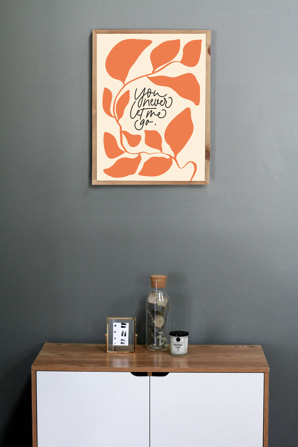 Der Spruch "You Never Lome to Go" auf einem modernen Wandbild in warmen Orangetönen, über einem Holz.
