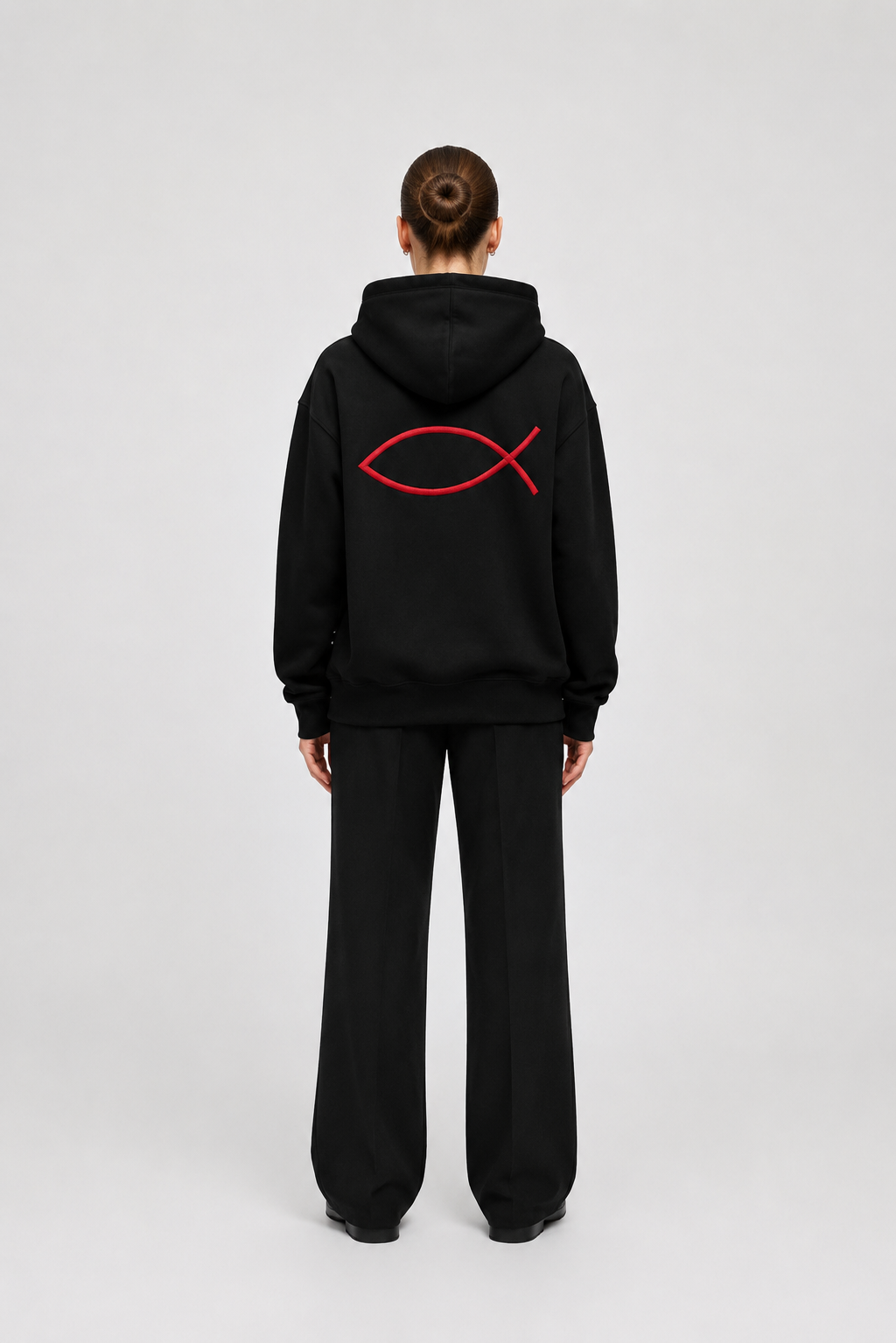 Ein Mensch trägt eine schwarze Kapuzenjacke mit rotem Fischsymbol, symbolisch für Christentum.