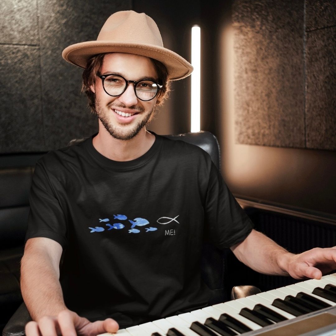 ME! gegen den Strom - aussagekräftiges T-Shirt Bio Baumwolle 12 Ein junger Mann mit Brille und Hut spielt Klavier, christliche Musik, kreative Atmosphäre.