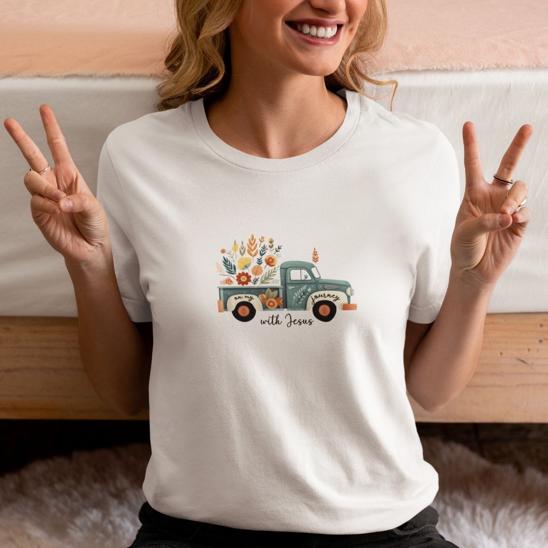 On my Journey with Jesus T-Shirt Bio Baumwolle 13 Ein lächelnder Frau trägt ein weißes T-Shirt mit einem bunten, floralen Truck-Design und dem Text "w.