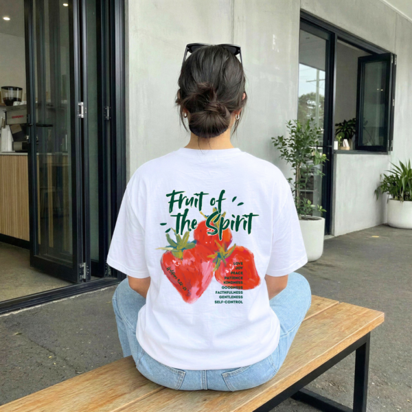 Person trägt T-Shirt mit Herz-Design und spirituellen Motiven vor modernem Gebäude.