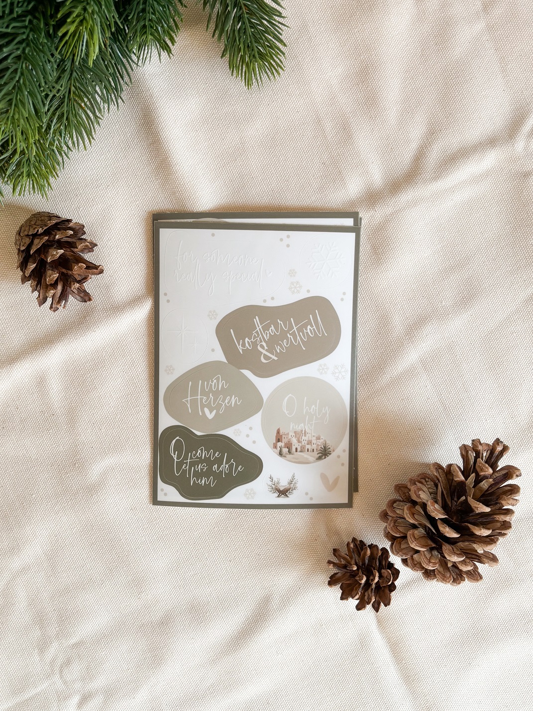 Stickerbogen »Christmas Blessings« 5 Christliche Grußkarten mit Weihnachtsmotiven auf Stoff, umgeben von Tannenzweigen und Zapfen.